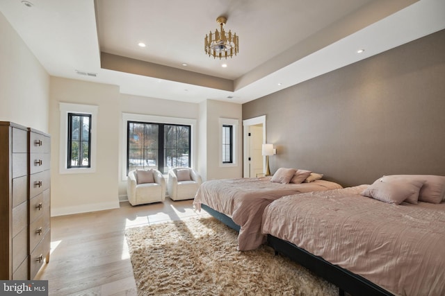 bedroom with a tray ceiling and light wood-type flooring