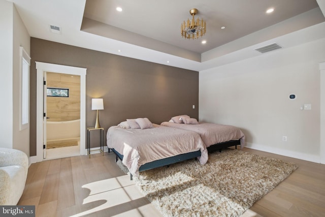 bedroom with connected bathroom, a tray ceiling, and light hardwood / wood-style flooring