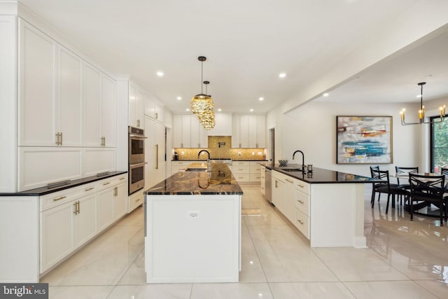 kitchen featuring white cabinetry, a center island with sink, a notable chandelier, pendant lighting, and stainless steel appliances