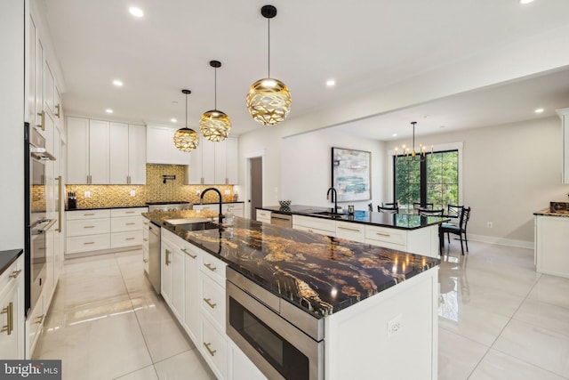 kitchen featuring sink, decorative backsplash, a large island with sink, hanging light fixtures, and stainless steel appliances