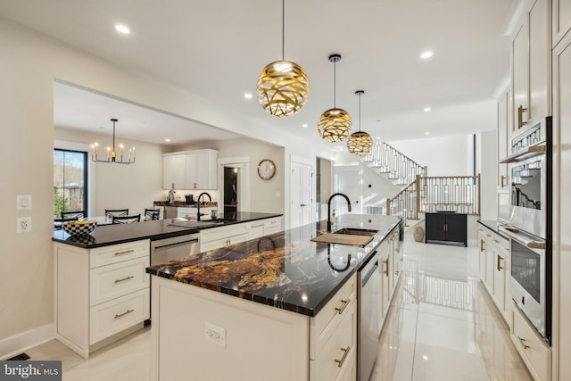 kitchen featuring sink, hanging light fixtures, stainless steel appliances, white cabinets, and a large island with sink