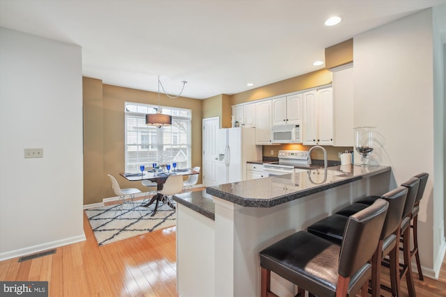 kitchen with white appliances, kitchen peninsula, a breakfast bar area, and white cabinets