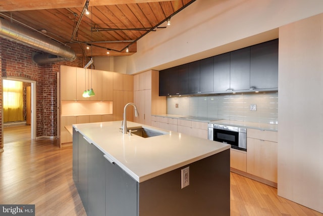 kitchen with brick wall, pendant lighting, an island with sink, sink, and oven