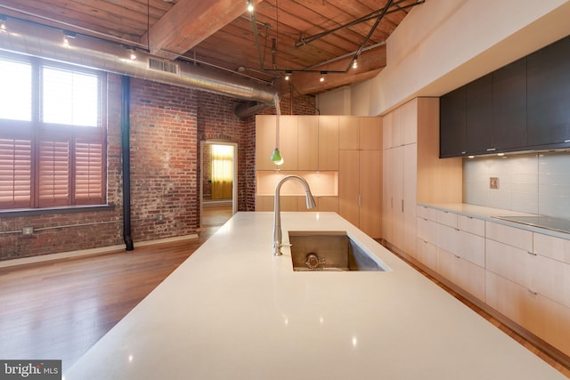 kitchen featuring brick wall, a towering ceiling, sink, hanging light fixtures, and light hardwood / wood-style floors