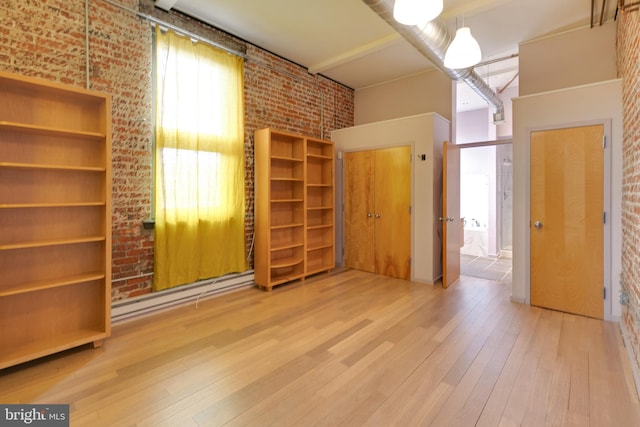 unfurnished bedroom with a baseboard heating unit, a towering ceiling, wood-type flooring, and brick wall