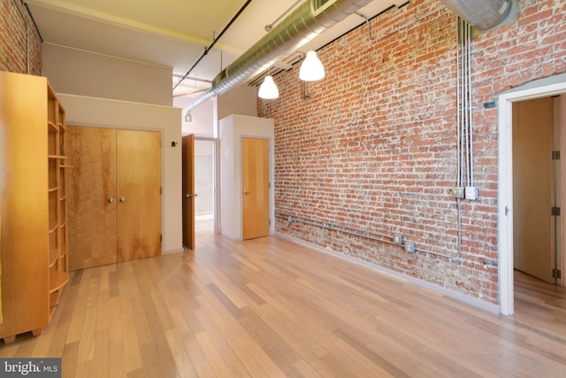 spare room featuring brick wall, a towering ceiling, and light hardwood / wood-style flooring