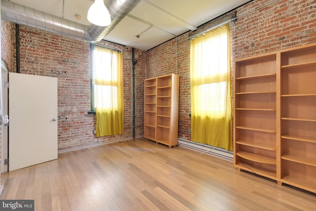 unfurnished room featuring hardwood / wood-style floors and brick wall