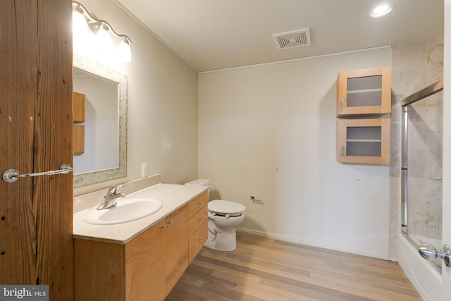 full bathroom with vanity, hardwood / wood-style floors, shower / bath combination with glass door, and toilet