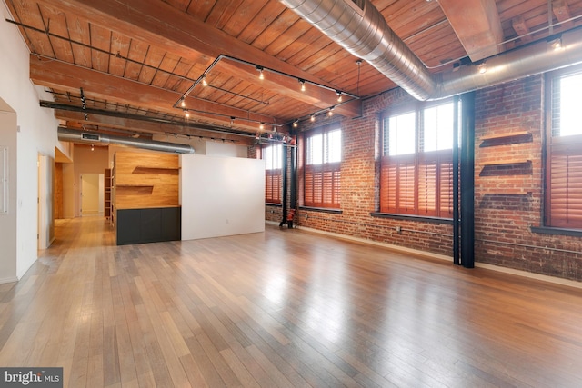 spare room with hardwood / wood-style flooring, track lighting, and brick wall