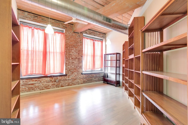 interior space featuring beamed ceiling, brick wall, and light hardwood / wood-style floors