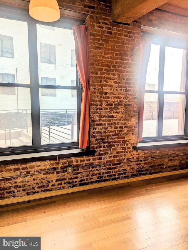 additional living space with hardwood / wood-style flooring, brick wall, and beam ceiling