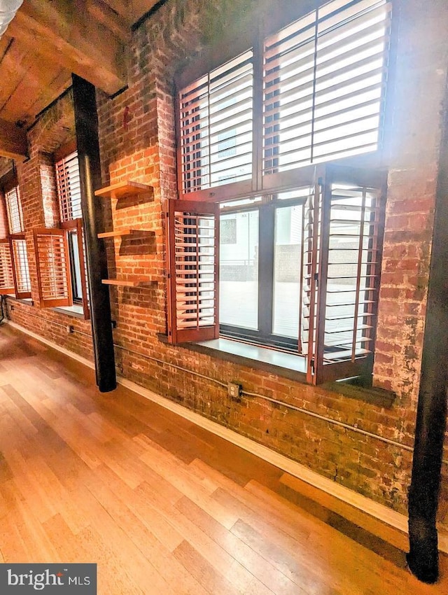 unfurnished living room with hardwood / wood-style flooring, brick wall, and beamed ceiling