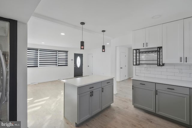 kitchen featuring gray cabinets, hanging light fixtures, decorative backsplash, and light hardwood / wood-style flooring