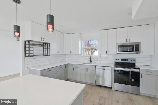 kitchen featuring stainless steel appliances, sink, hanging light fixtures, and light wood-type flooring