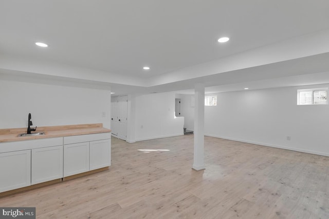 basement featuring sink, electric panel, and light hardwood / wood-style flooring