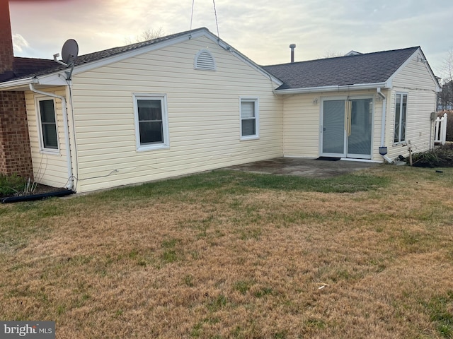 back house at dusk with a patio and a lawn