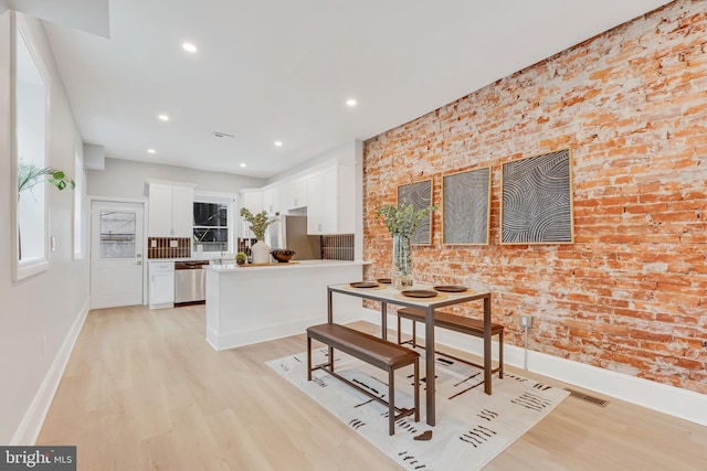 dining room featuring brick wall and light wood-type flooring