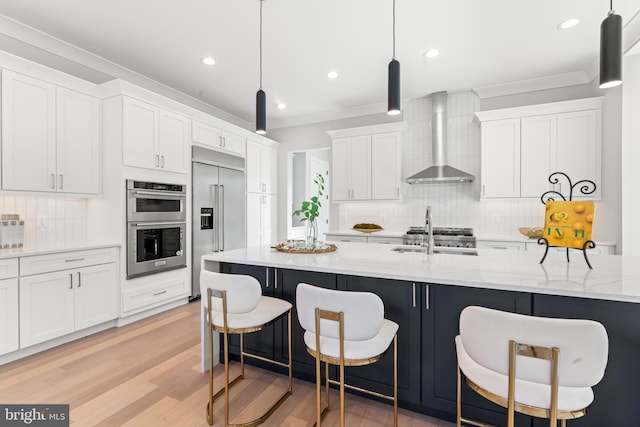 kitchen featuring sink, wall chimney range hood, pendant lighting, stainless steel appliances, and white cabinets