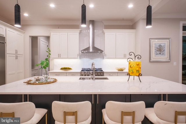 kitchen featuring wall chimney exhaust hood, hanging light fixtures, and a large island with sink