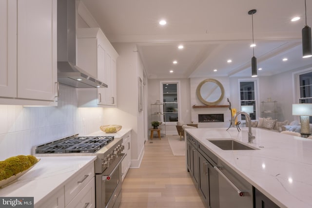 kitchen featuring wall chimney exhaust hood, light stone counters, appliances with stainless steel finishes, pendant lighting, and white cabinets