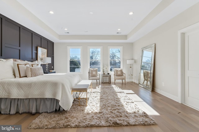 bedroom with multiple windows, light hardwood / wood-style floors, and a tray ceiling