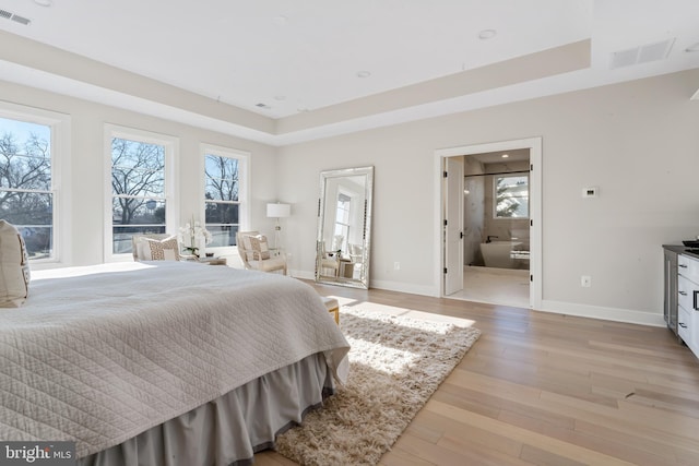 bedroom with connected bathroom, a tray ceiling, and light hardwood / wood-style floors