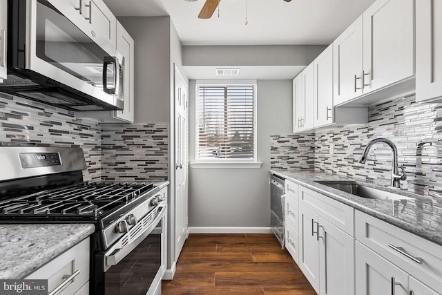 kitchen with sink, appliances with stainless steel finishes, dark hardwood / wood-style floors, light stone counters, and white cabinets