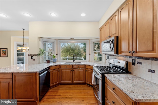 kitchen with appliances with stainless steel finishes, sink, backsplash, light hardwood / wood-style floors, and kitchen peninsula