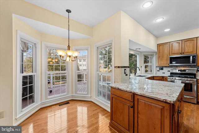 kitchen with sink, hanging light fixtures, stainless steel appliances, light stone countertops, and kitchen peninsula