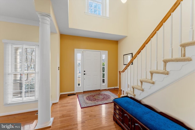 entrance foyer with crown molding, decorative columns, light hardwood / wood-style floors, and a towering ceiling