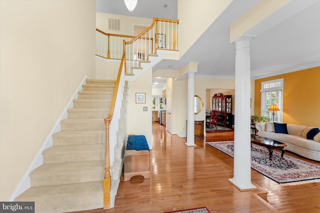 staircase with wood-type flooring, decorative columns, and a high ceiling