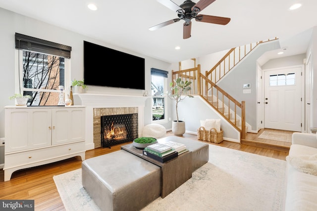 living room featuring ceiling fan, a fireplace, and light wood-type flooring