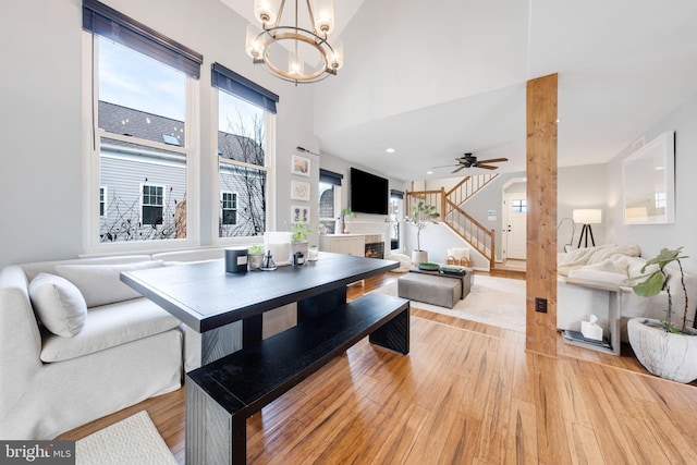 dining area with ceiling fan with notable chandelier, light hardwood / wood-style floors, and a high ceiling