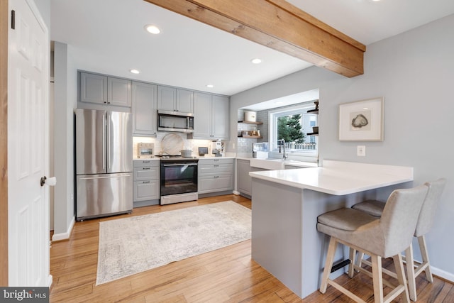 kitchen featuring gray cabinetry, a breakfast bar area, kitchen peninsula, and appliances with stainless steel finishes