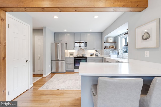 kitchen with sink, gray cabinetry, stainless steel appliances, a kitchen bar, and kitchen peninsula