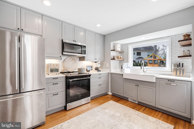 kitchen with appliances with stainless steel finishes, tasteful backsplash, sink, gray cabinetry, and light wood-type flooring