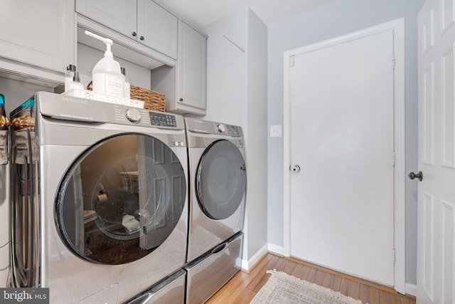 clothes washing area featuring washing machine and dryer, cabinets, and light wood-type flooring