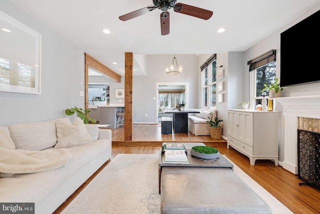 living room featuring a fireplace, ceiling fan with notable chandelier, and light hardwood / wood-style flooring