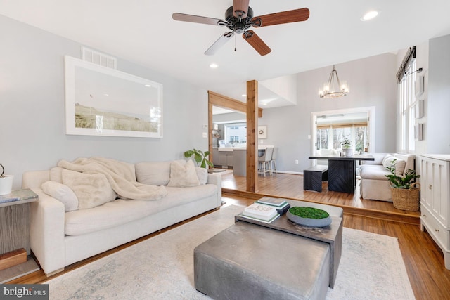 living room with ceiling fan with notable chandelier and light hardwood / wood-style floors