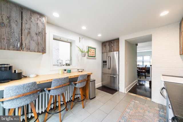 kitchen with butcher block countertops, stainless steel fridge with ice dispenser, and light tile patterned floors