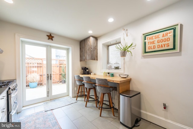 kitchen with a breakfast bar, butcher block counters, light tile patterned flooring, stainless steel range with gas cooktop, and french doors