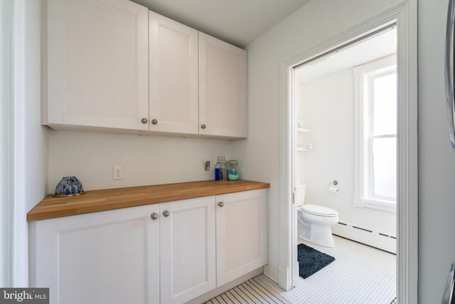 interior space featuring wood counters, a baseboard heating unit, white cabinetry, and light tile patterned floors