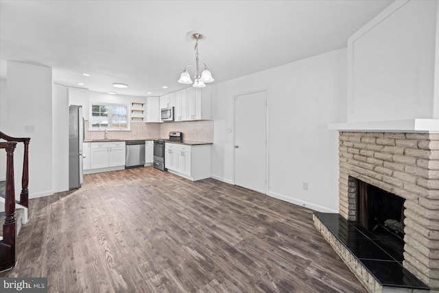 kitchen with decorative light fixtures, white cabinets, backsplash, stainless steel appliances, and a brick fireplace