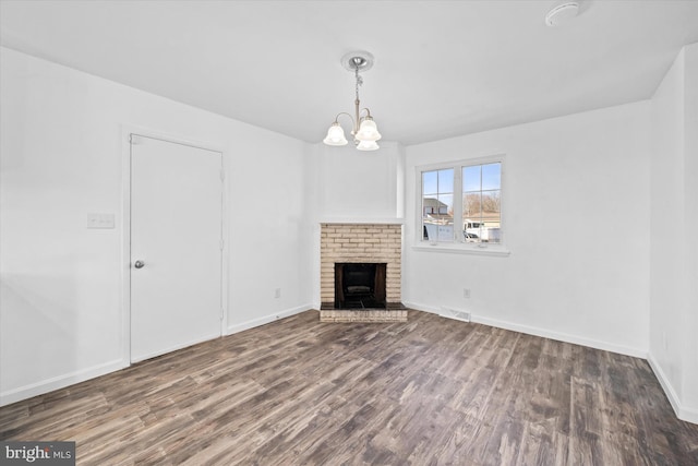 unfurnished living room featuring a brick fireplace, dark hardwood / wood-style floors, and a notable chandelier