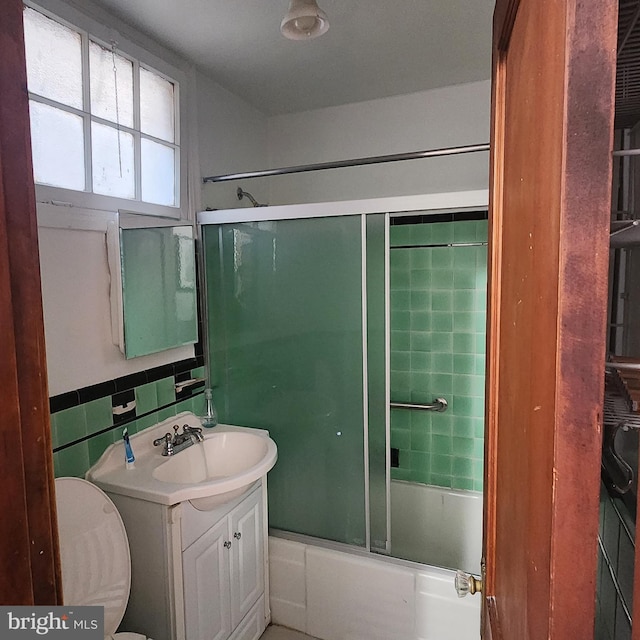 full bathroom with vanity, toilet, combined bath / shower with glass door, and tile walls