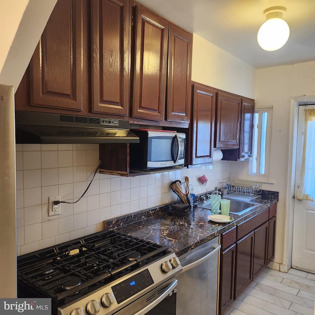 kitchen with dark brown cabinetry, sink, dark stone counters, stainless steel appliances, and backsplash