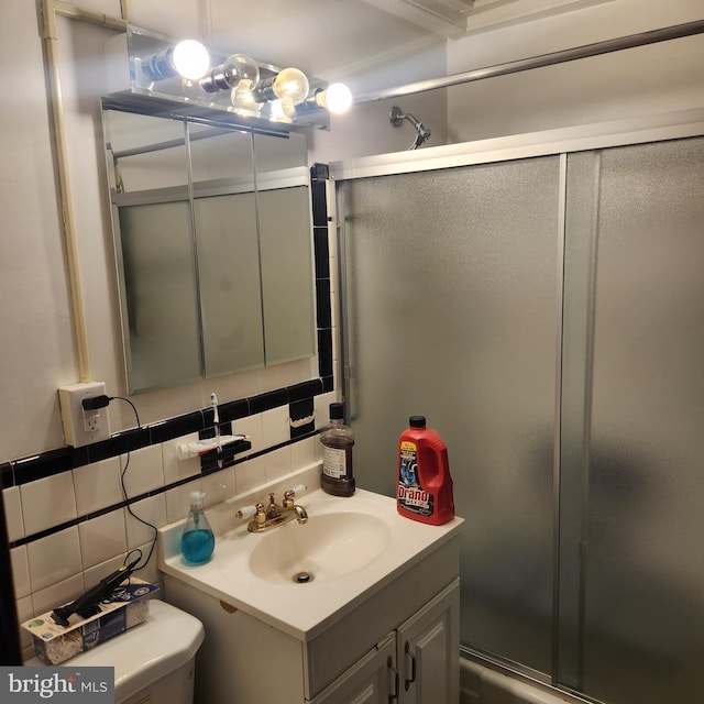 bathroom with toilet, a shower with shower door, tile walls, vanity, and decorative backsplash