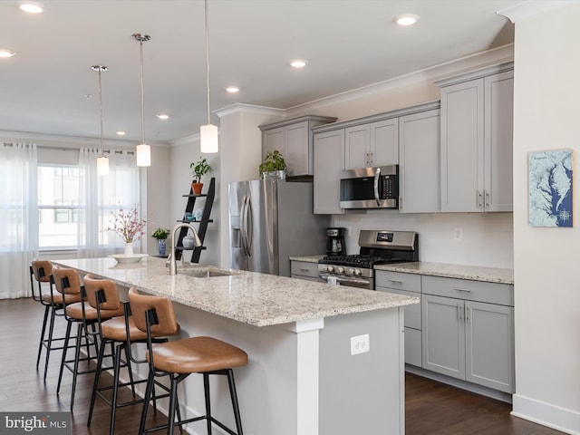 kitchen with a kitchen bar, light stone counters, decorative light fixtures, appliances with stainless steel finishes, and an island with sink