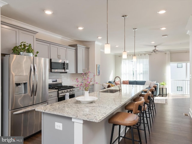 kitchen with light stone counters, tasteful backsplash, hanging light fixtures, appliances with stainless steel finishes, and an island with sink