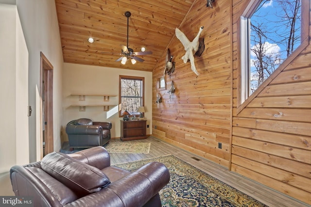 sitting room with wood walls, wood-type flooring, lofted ceiling, ceiling fan, and wood ceiling